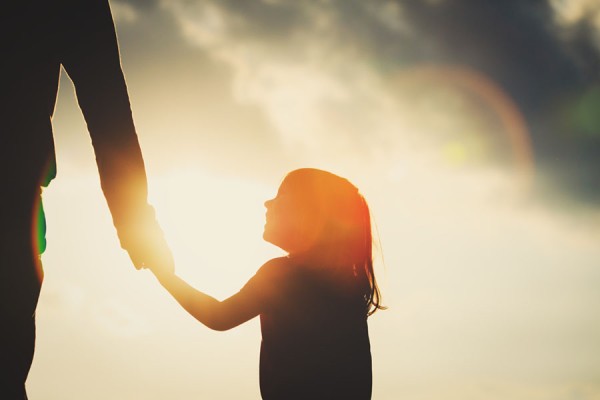 silhouette of little girl holding parent hand at sunset
